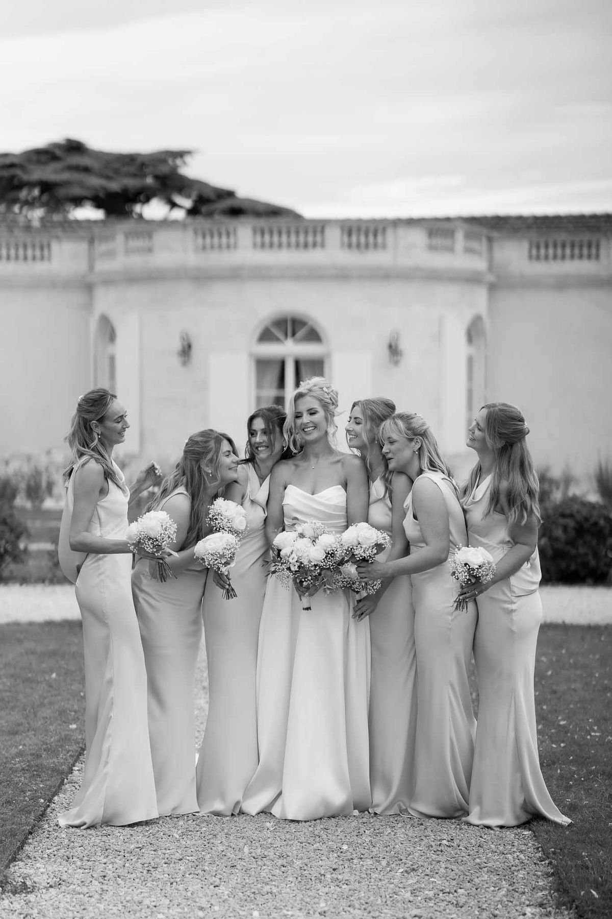 Bride and bridesmaids group portrait in front of classical stone building with white bouquets