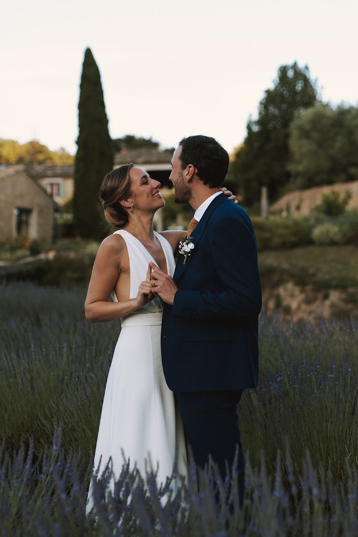 Bride in white V-neck gown and groom in navy suit with mustard tie in lavender field at golden hour