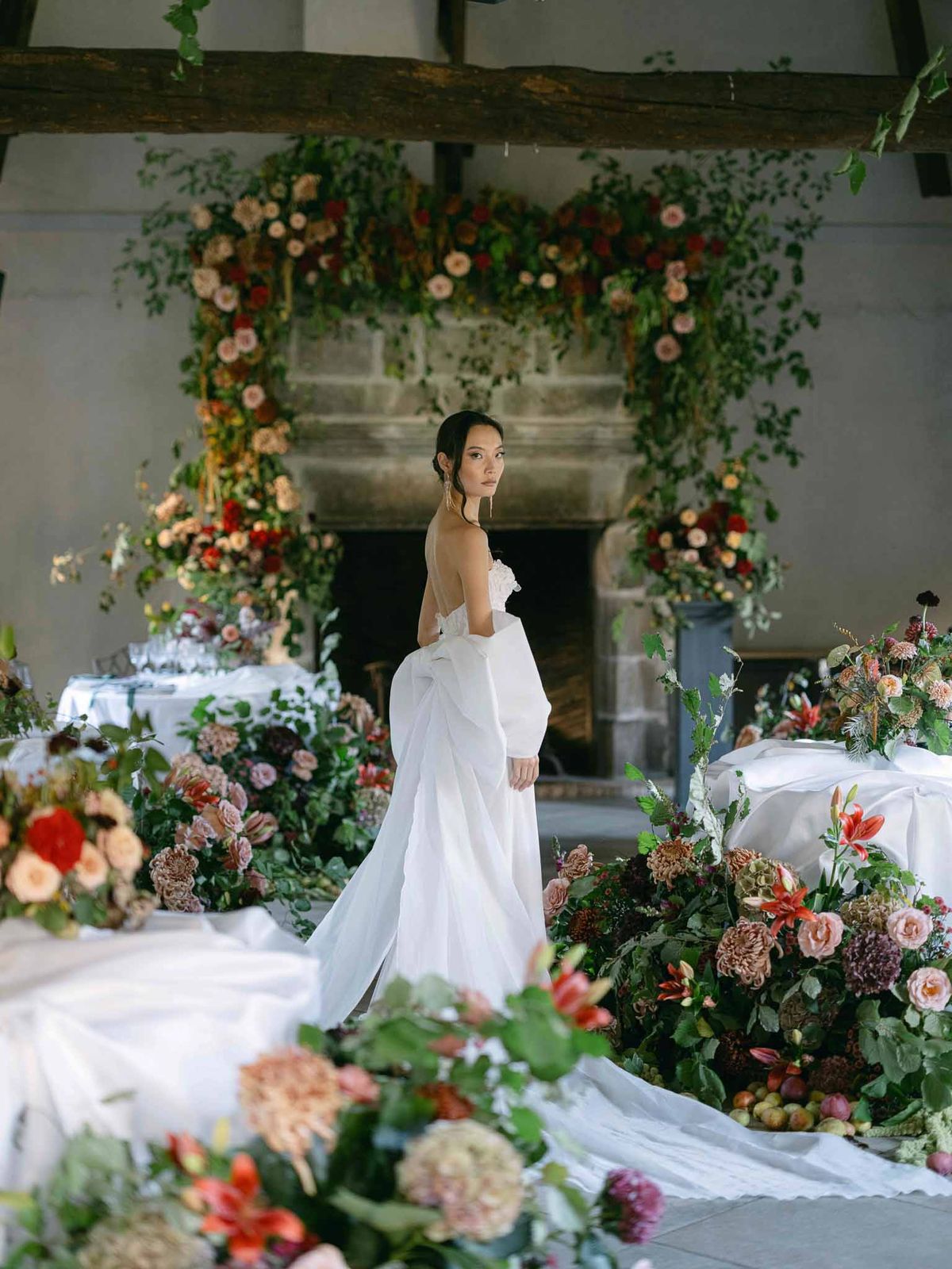 Bride in strapless gown with oversized bow standing among reception tables with autumn floral arrangements in a chateau
