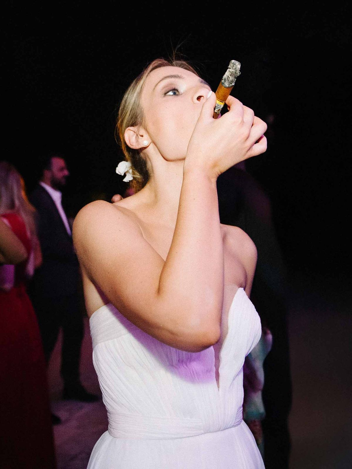 Bride smoking cigar during evening wedding reception with purple ambient lighting