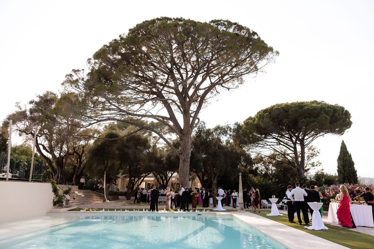 Forty guests mingling at poolside cocktail hour with candlelit pool edge and lit villa pavilion at dusk
