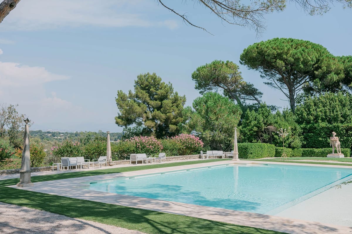 Rectangular pool with cream stone surround, sculptural pedestals, and oleander hedging at estate