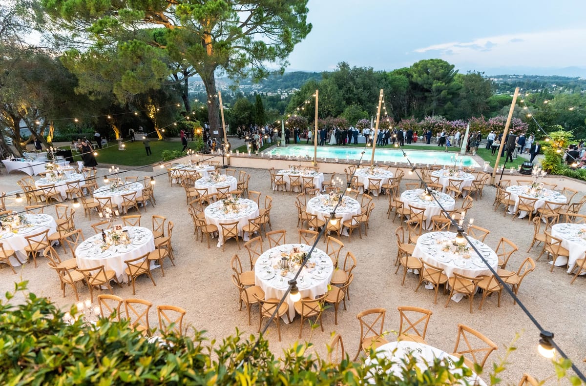 Aerial dusk view of 15 round reception tables with Edison lights and pool cocktail hour on hillside