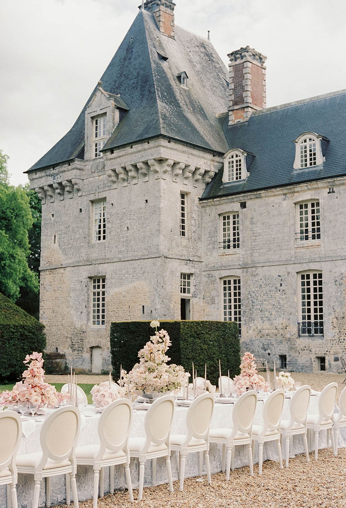 Elegant outdoor reception table setting at French stone château with blush florals and cream chairs