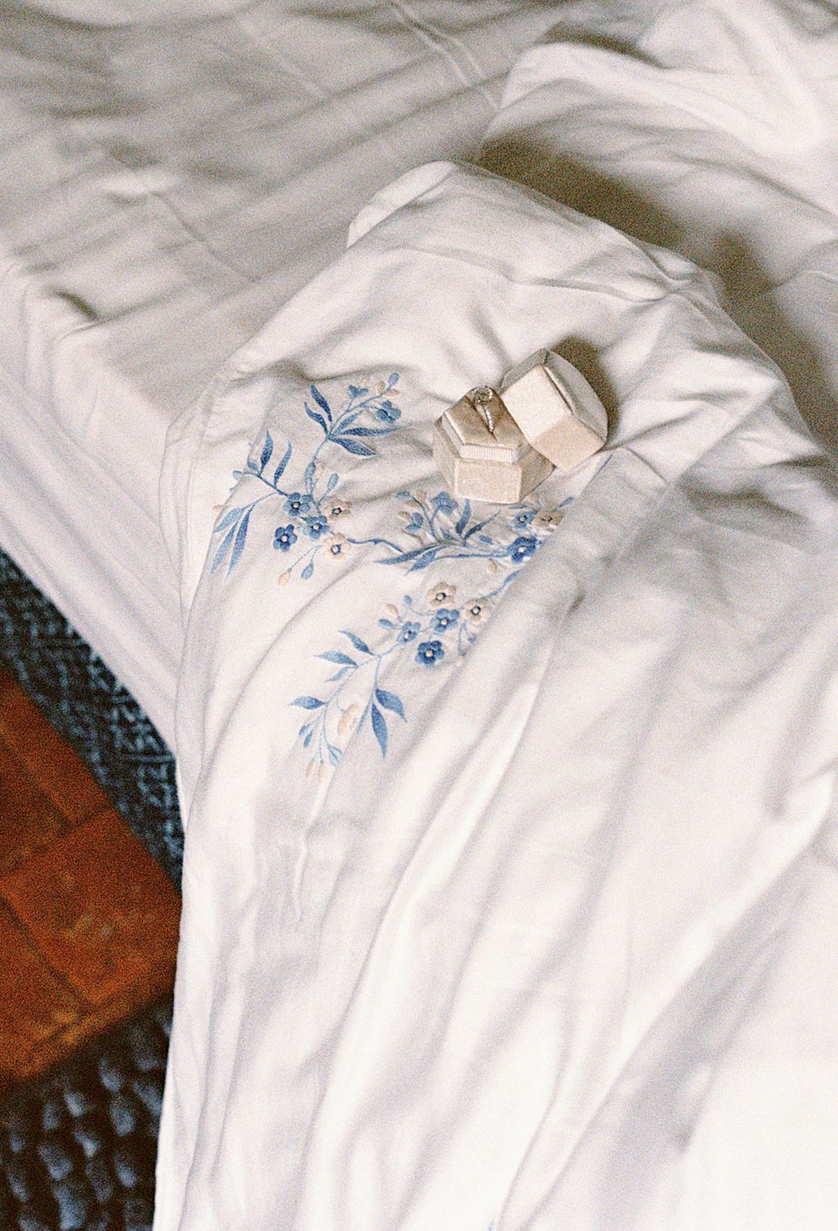 Close-up flat lay of ivory wedding dress with blue embroidered florals and gold wedding ring