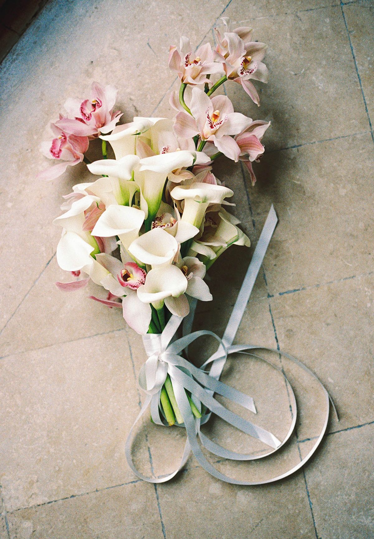 White calla lily and blush cymbidium orchid bouquet with silver satin ribbon on stone tile floor