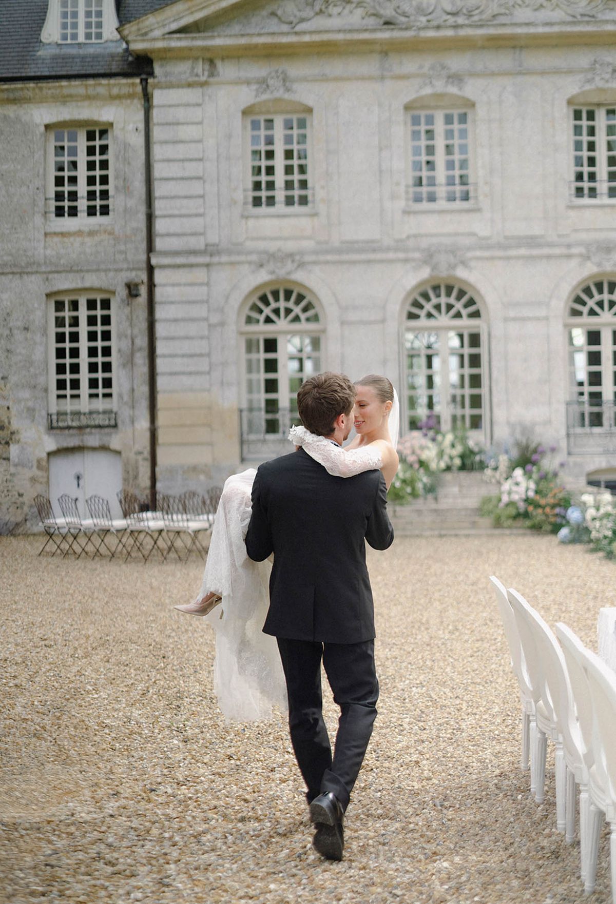 Groom carrying bride through courtyard at Georgian stone manor house wedding venue
