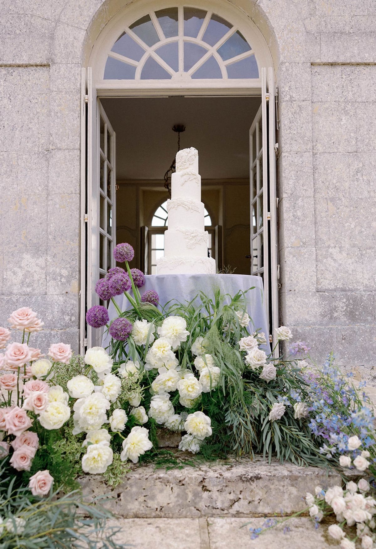 Four-tier white wedding cake with floral arrangements in classical stone doorway entrance