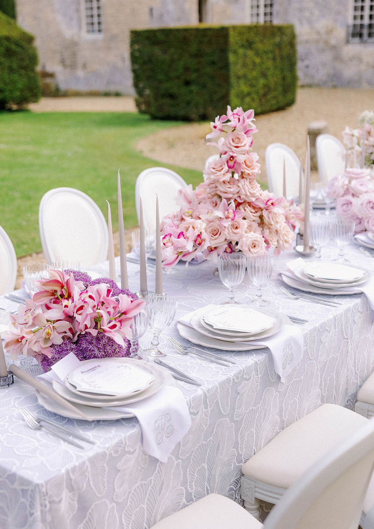 Elegant outdoor reception table setting with floral centerpieces at château garden courtyard
