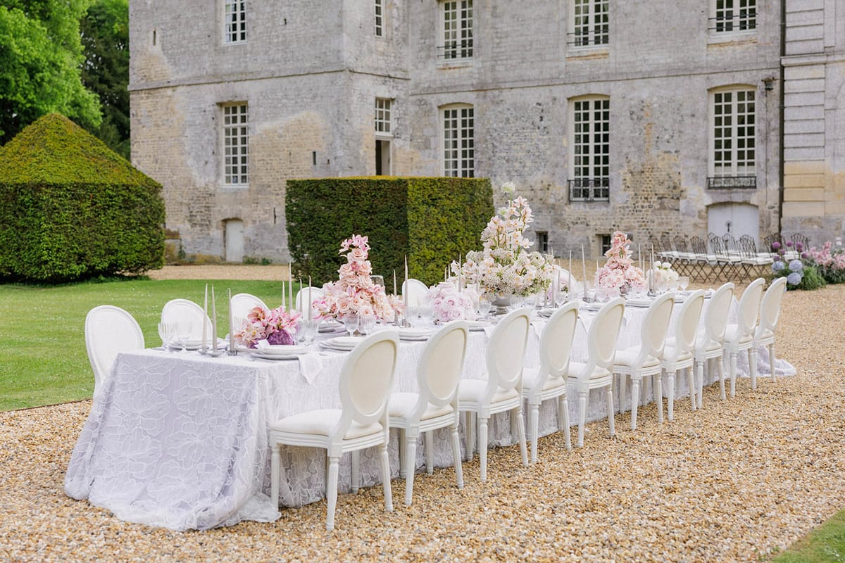 Wedding reception table setting in château courtyard with floral centerpieces and formal garden backdrop