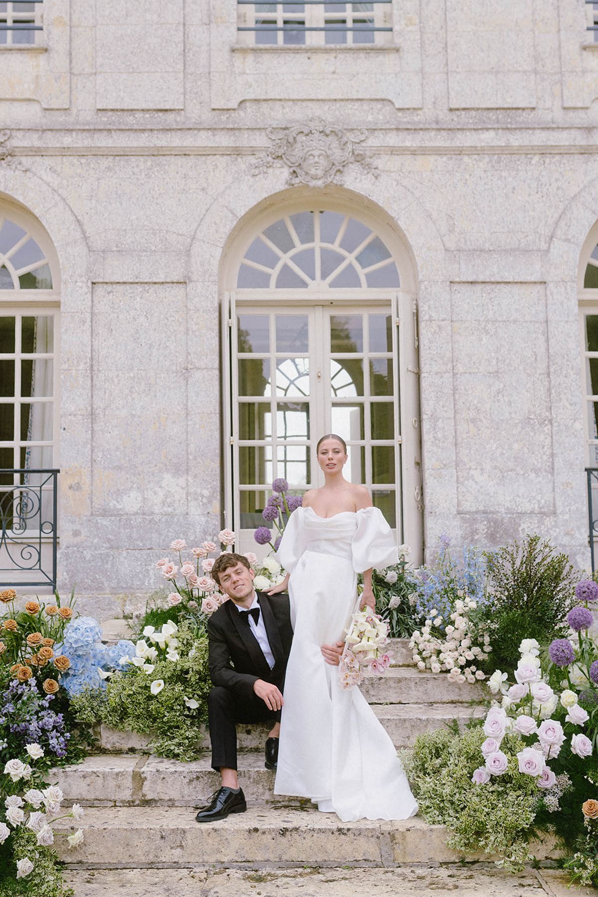 Bride and groom portrait outside classical stone building with floral arrangements