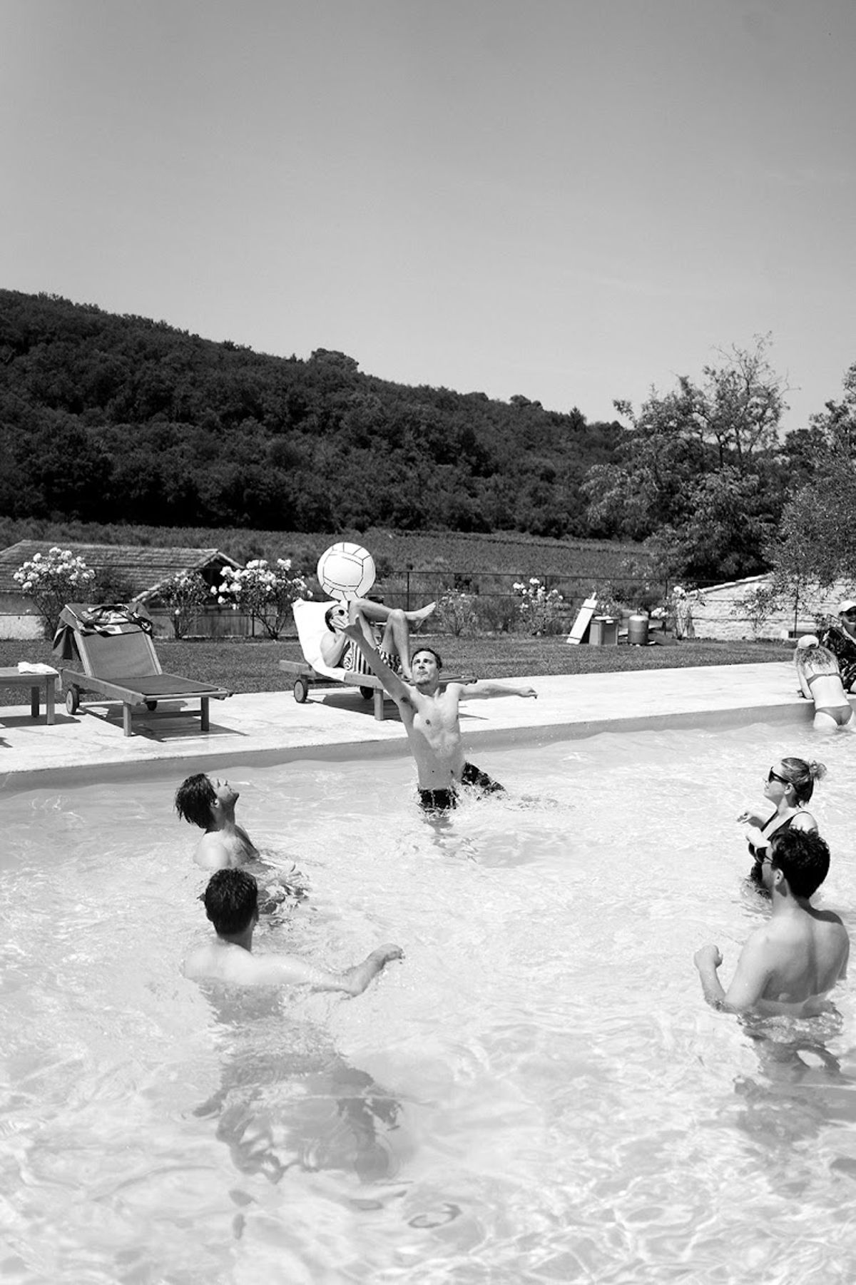 Guests playing in outdoor pool with inflatable ball during wedding weekend gathering in B&W