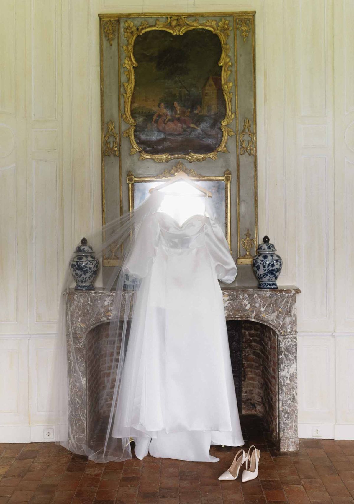 Bride in ivory wedding dress and veil posing before ornate marble fireplace in neoclassical interior