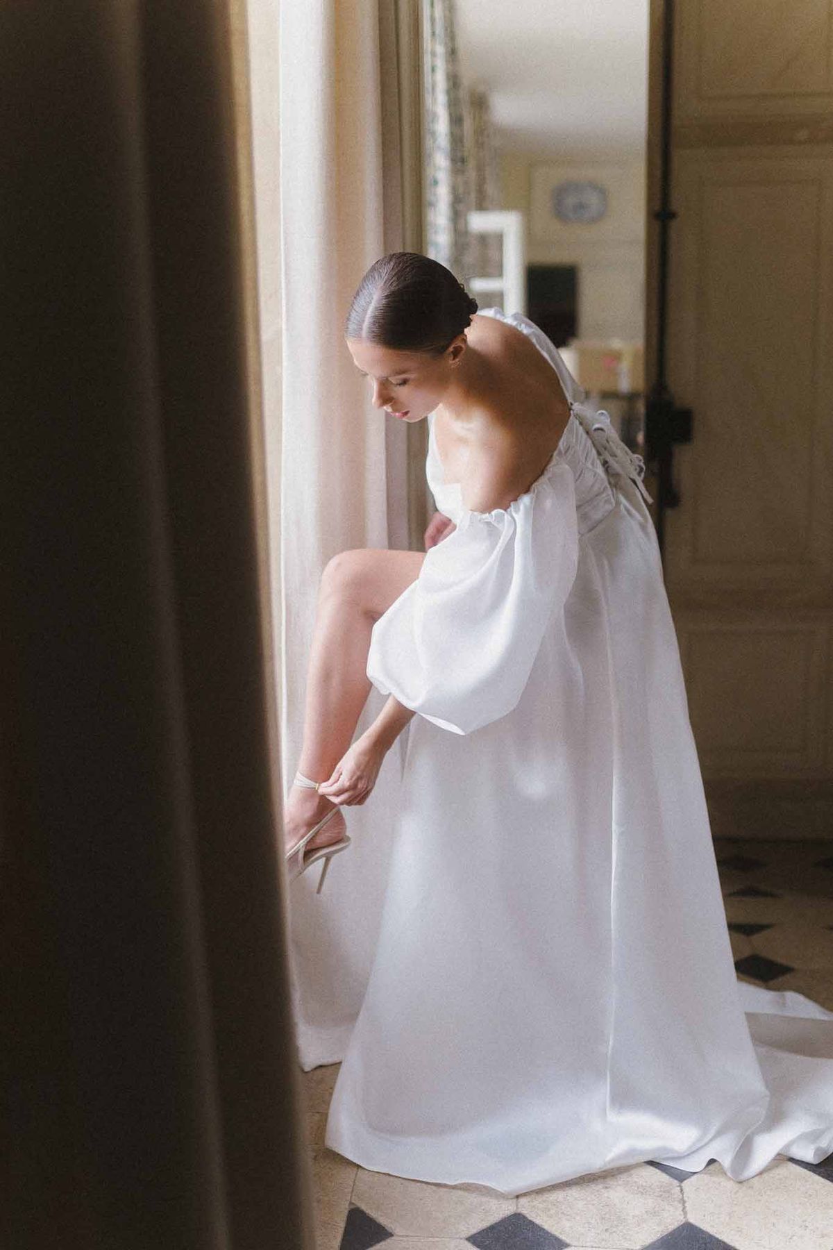 Bride adjusting shoes in classical interior hallway during getting ready preparations