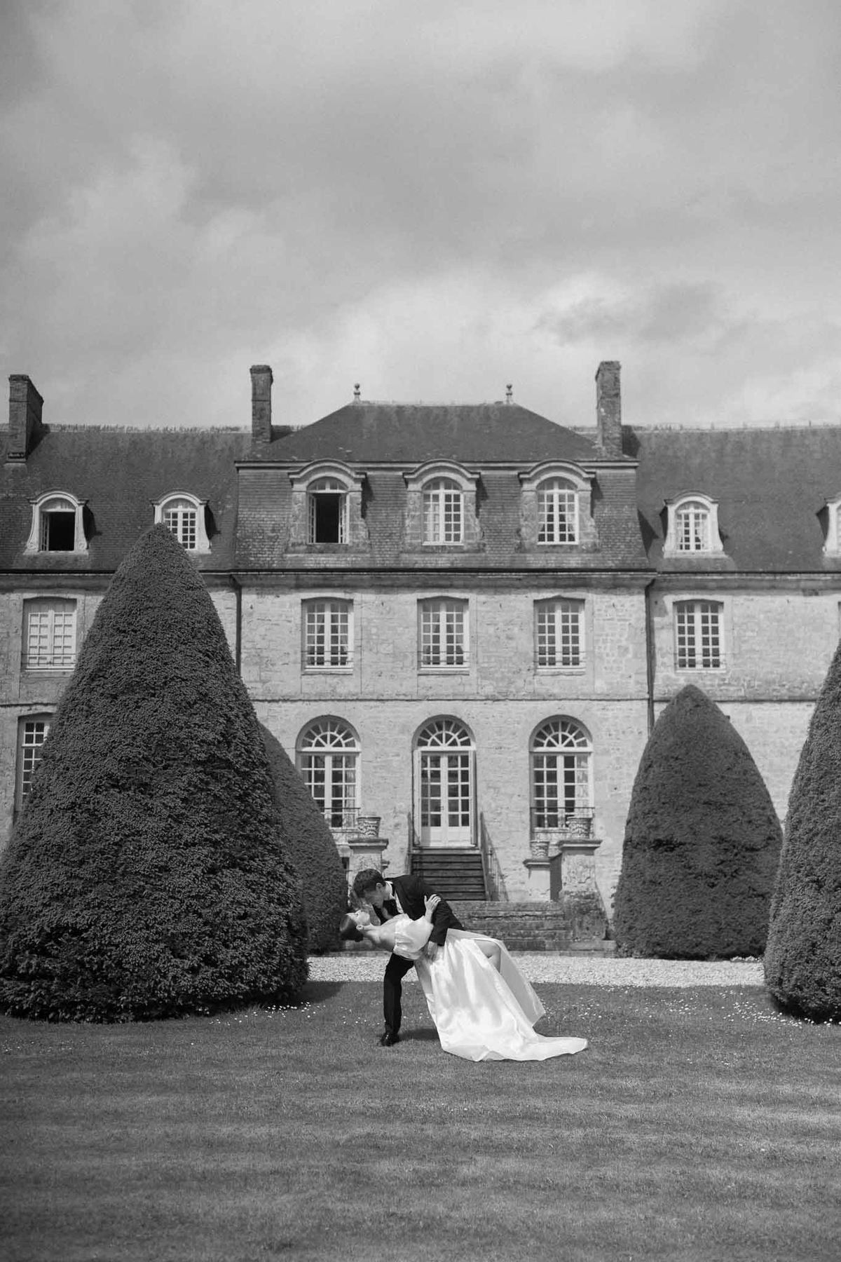 Bride and groom romantic dip pose between topiary cones at French château garden
