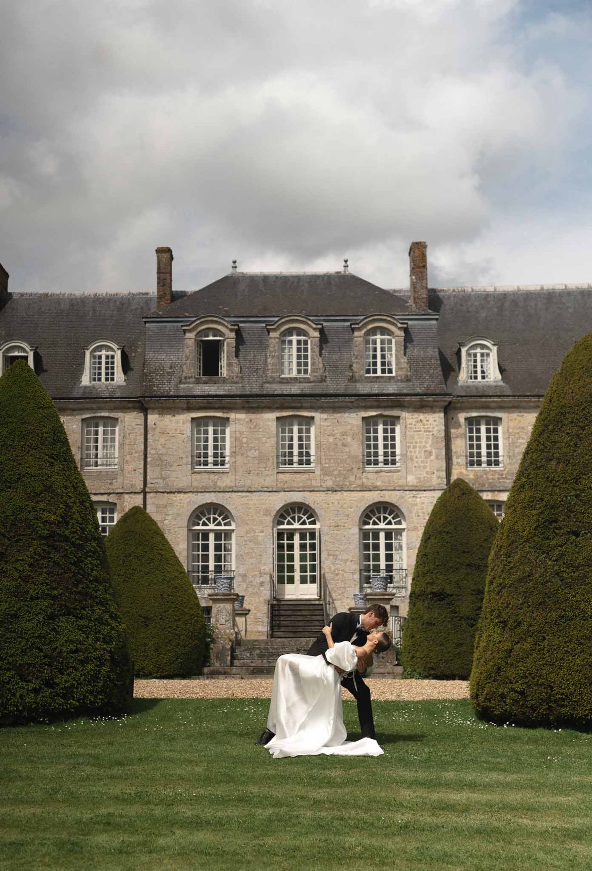 Bride and groom romantic dip kiss portrait at French château estate with formal gardens