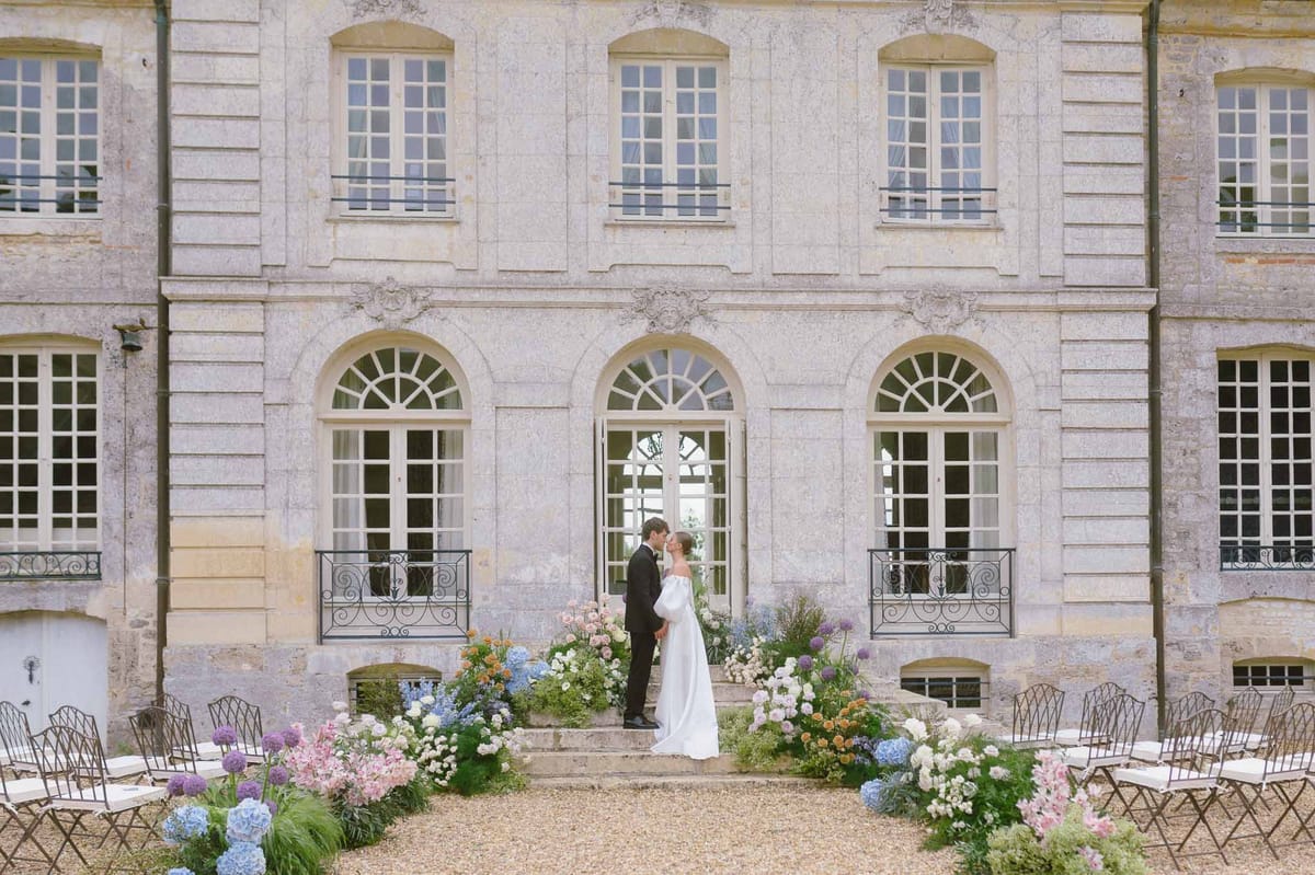 Bride and groom ceremony at French stone château with floral arrangements and courtyard seating