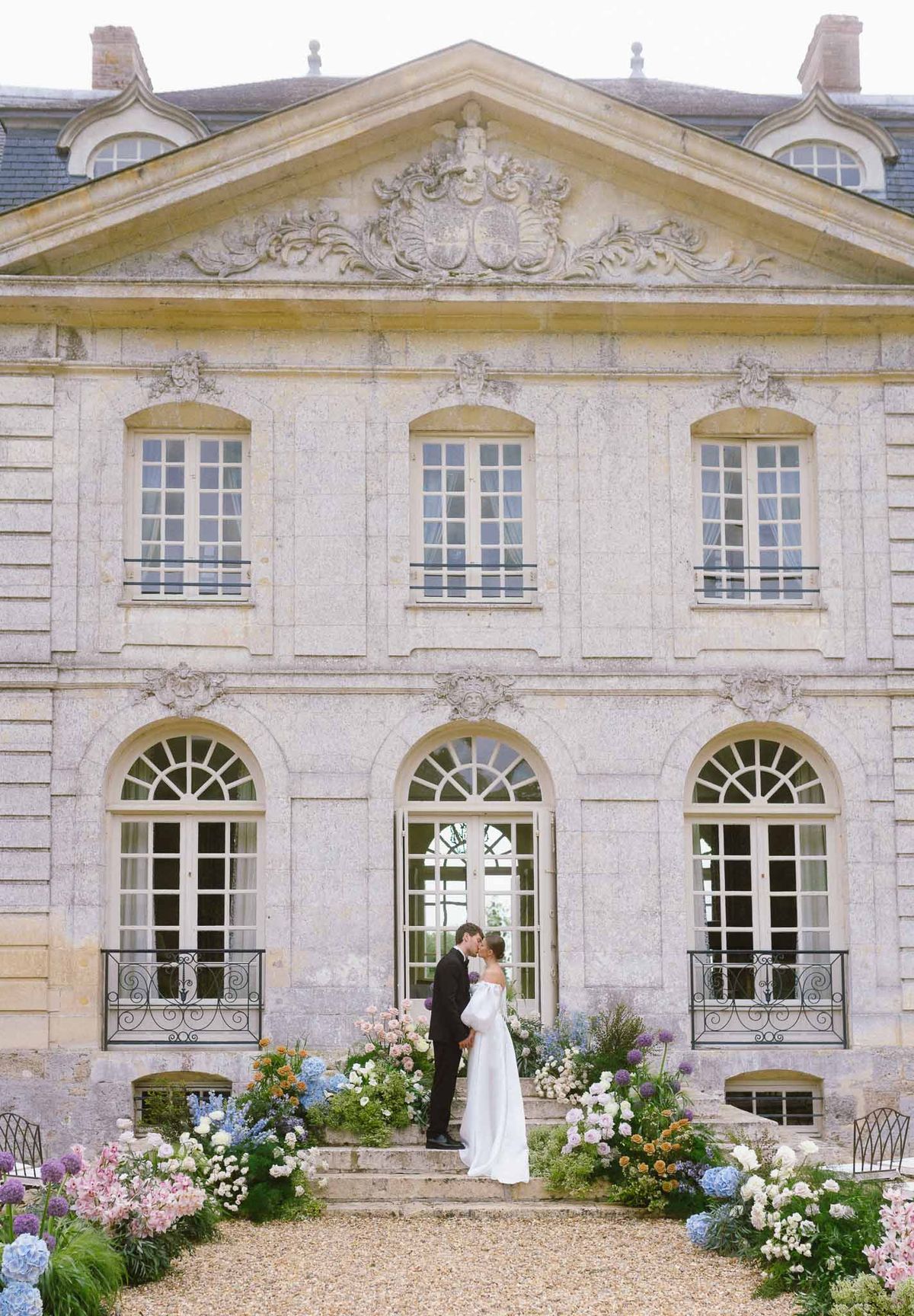 Couple kissing on chateau entrance steps flanked by blue hydrangea and pink rose ground installations
