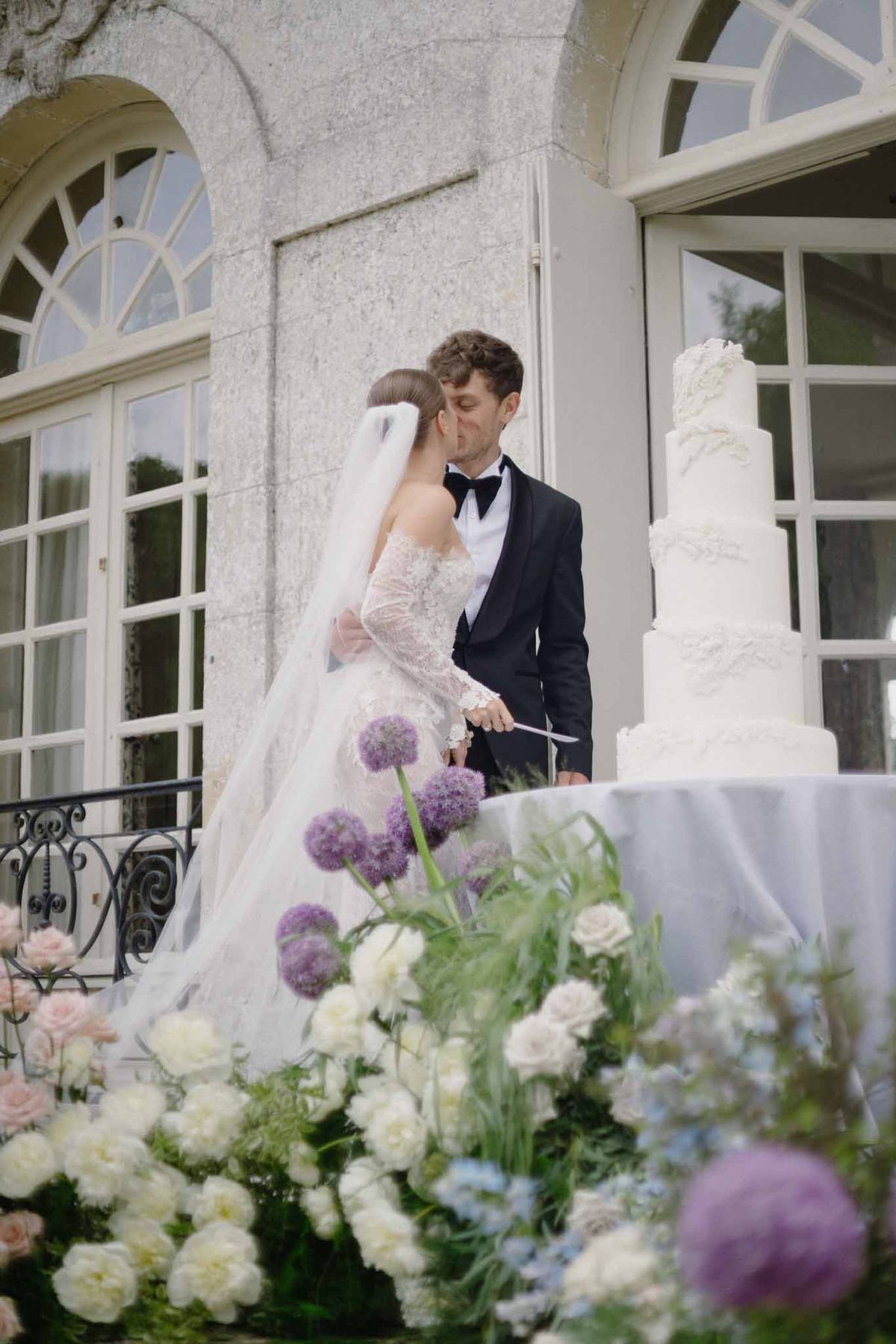 Bride and groom cutting wedding cake on stone terrace at classical venue reception