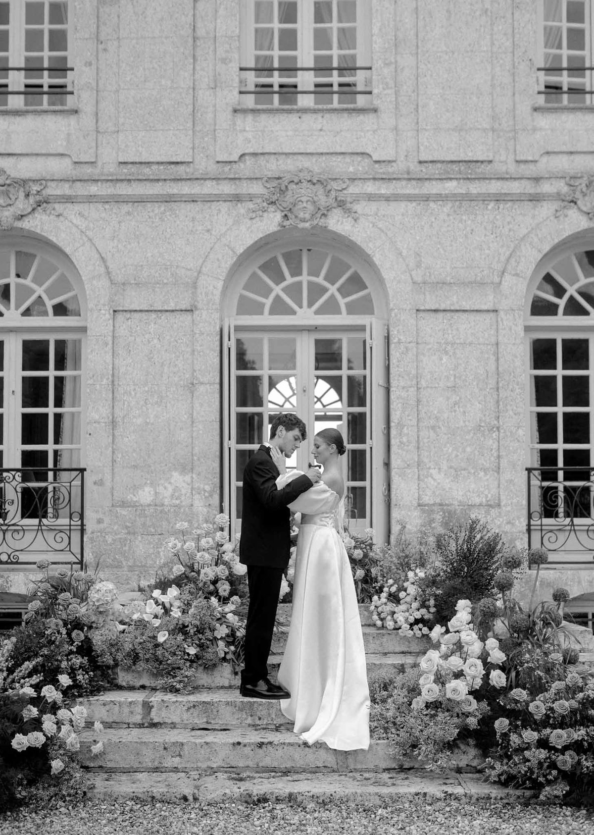 Bride and groom portrait in classical stone courtyard with arched windows and floral arrangements