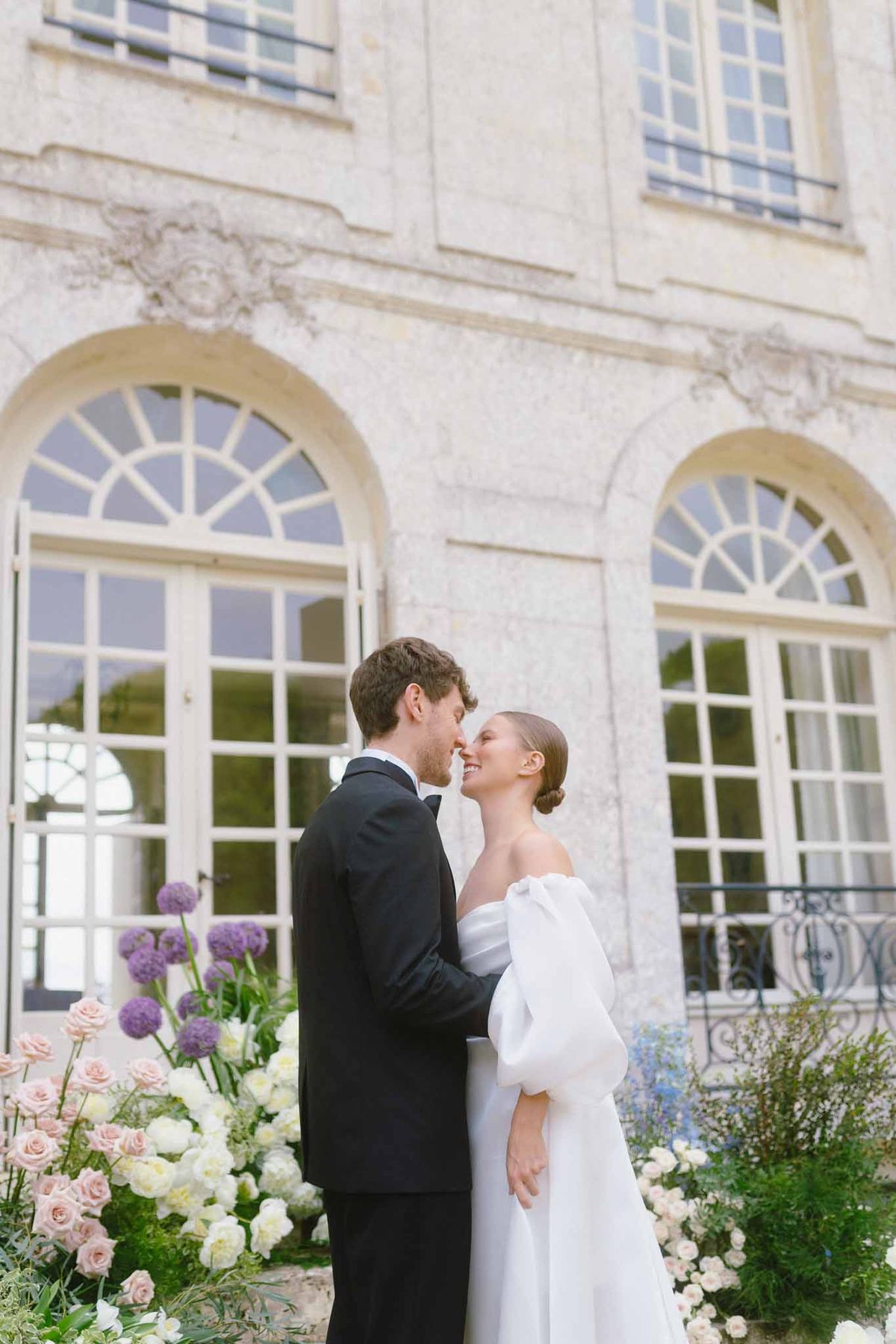 Bride and groom portrait against classical stone building with arched windows and floral arrangements