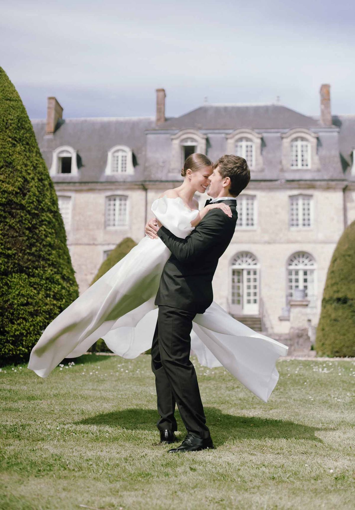 Groom lifts bride in romantic portrait moment on formal French château grounds with sculpted hedges