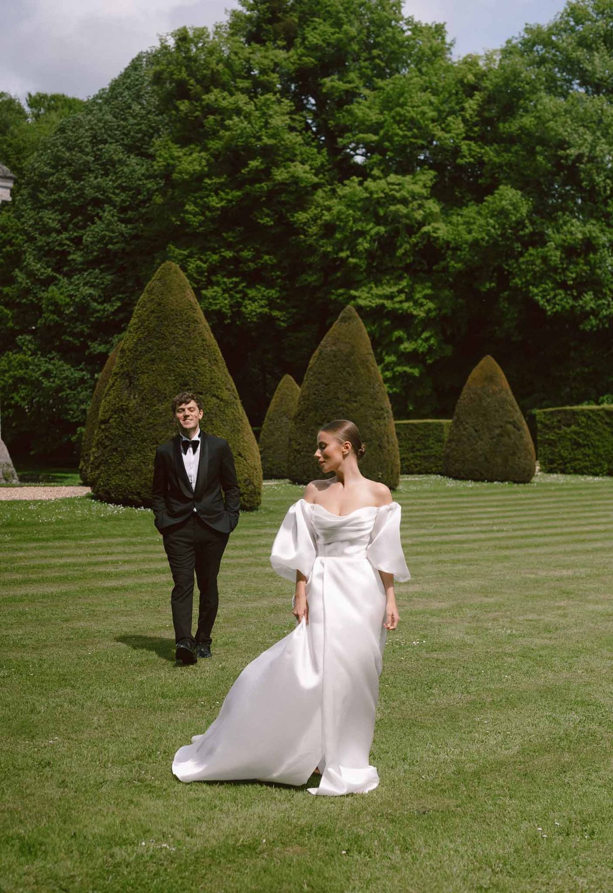 Bride and groom pose together in formal garden with topiary hedges