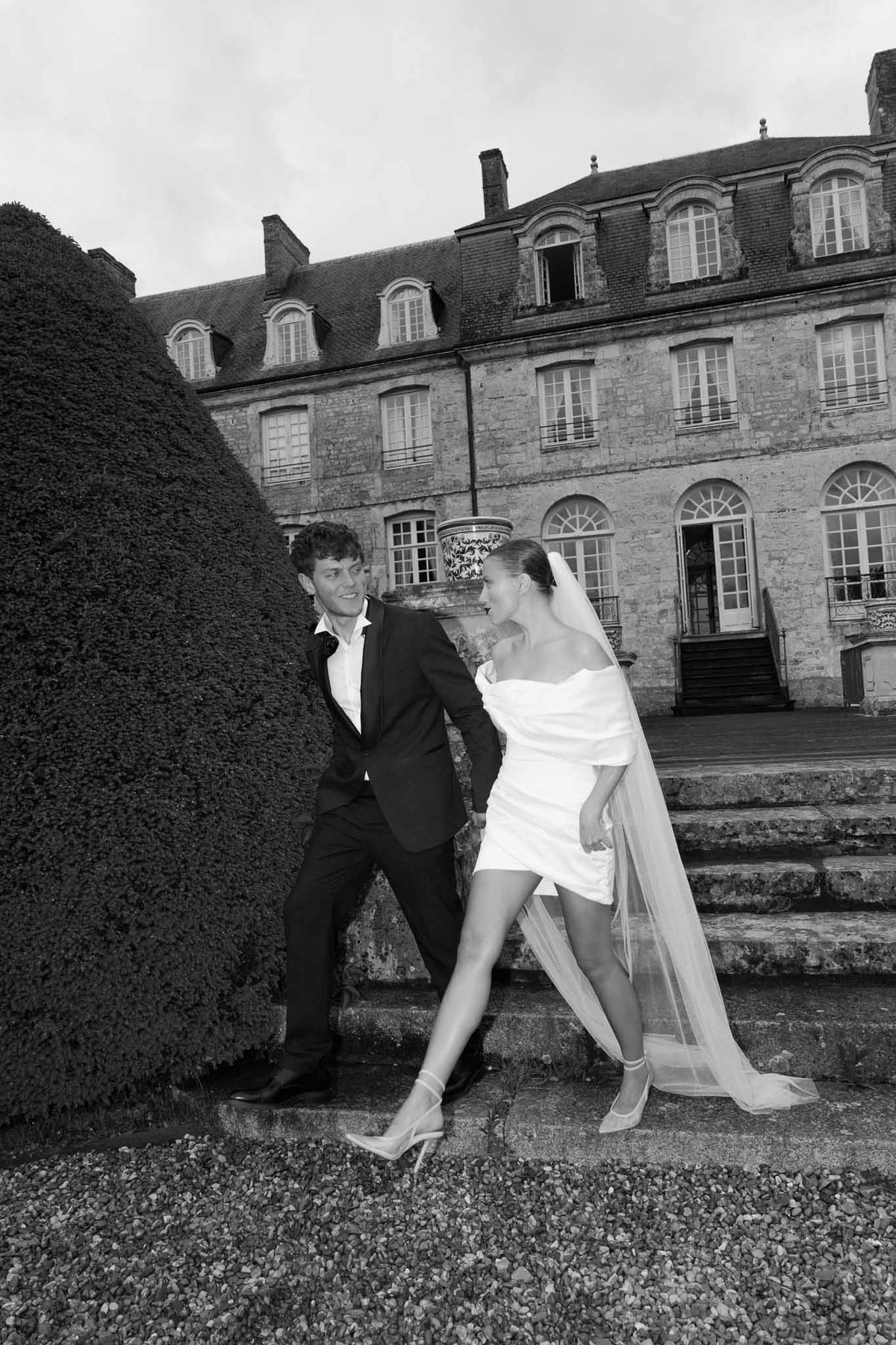 Bride and groom portrait in front of classical stone manor house with formal gardens
