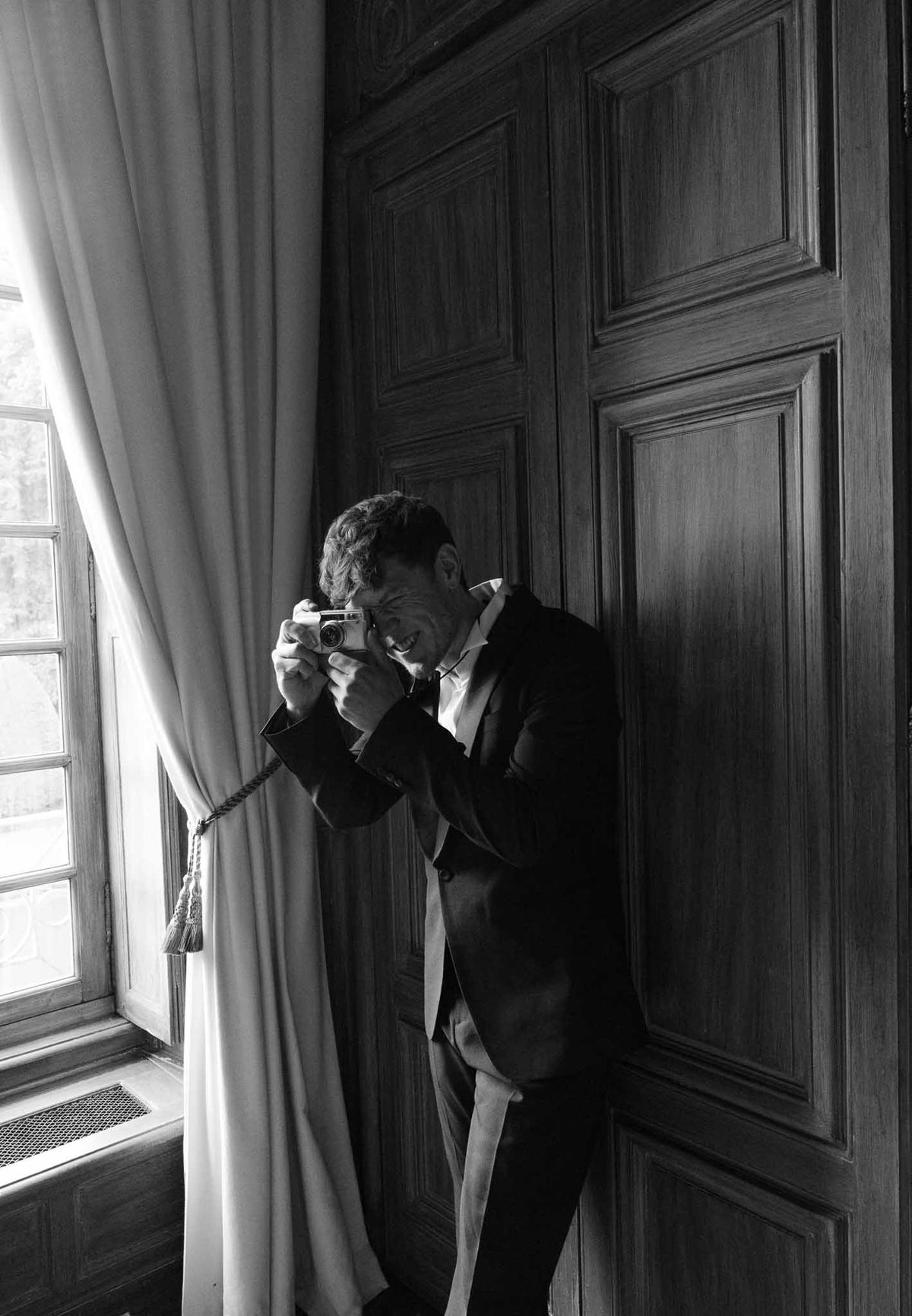 Groom adjusting cufflinks by window during wedding preparation in elegant wood-paneled room