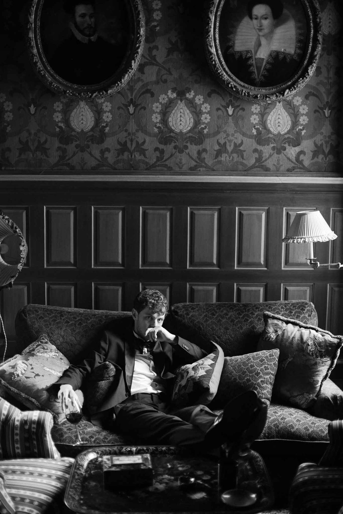 Groom in contemplative moment seated on patterned sofa in classical interior room