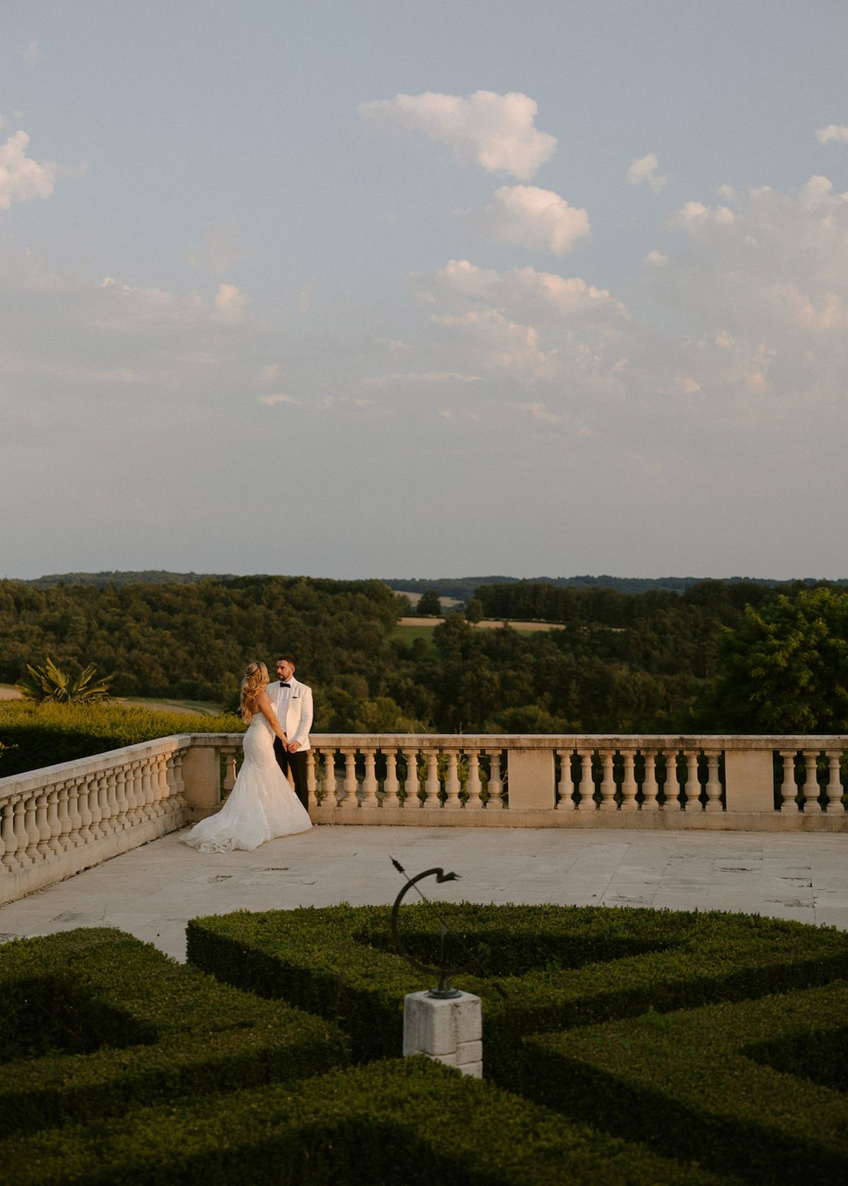 Couple holding hands at chateau balustrade overlooking countryside with parterre garden at golden hour