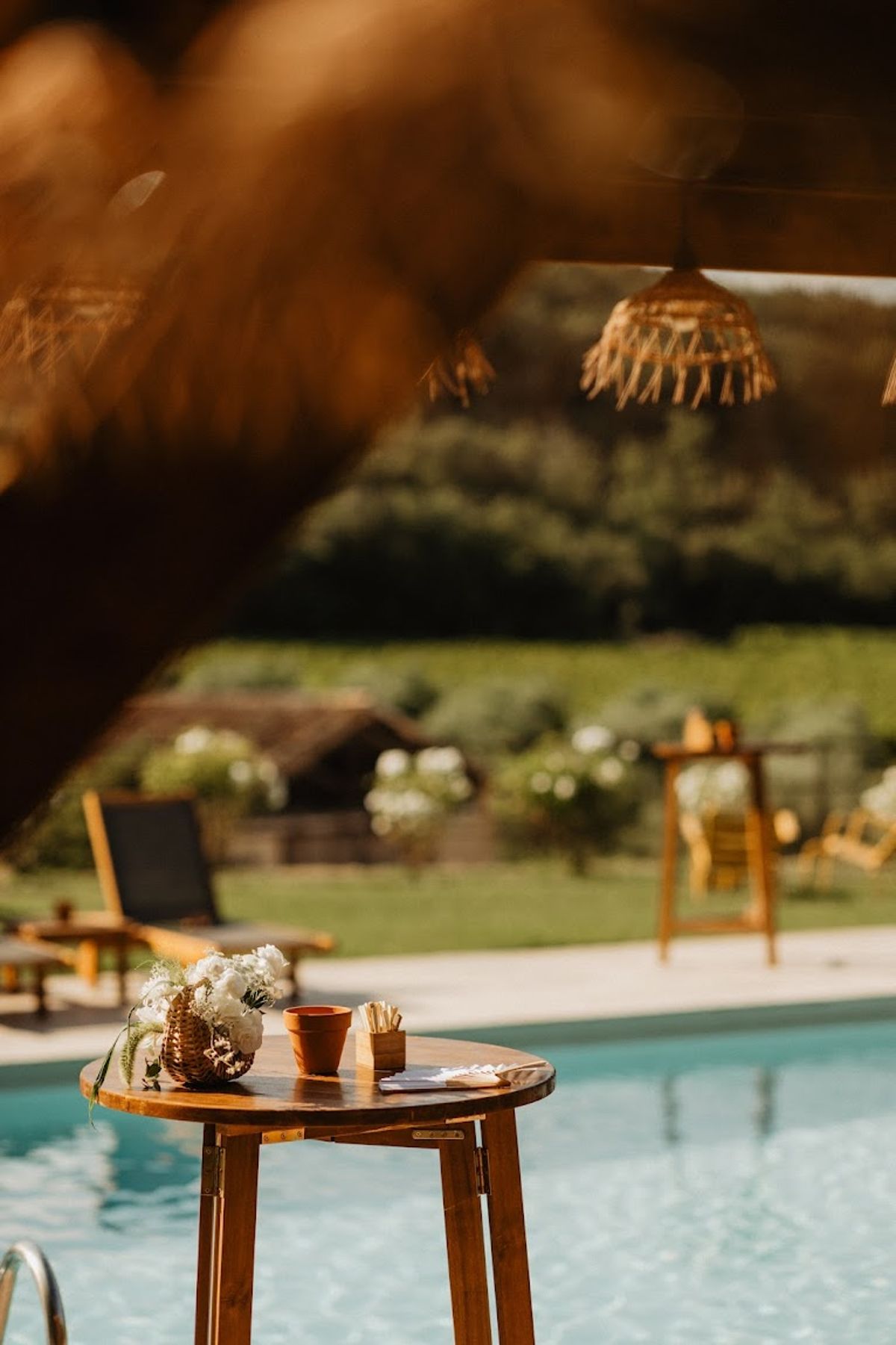 Poolside cocktail hour high-top table with copper vessel florals and rattan pendant light