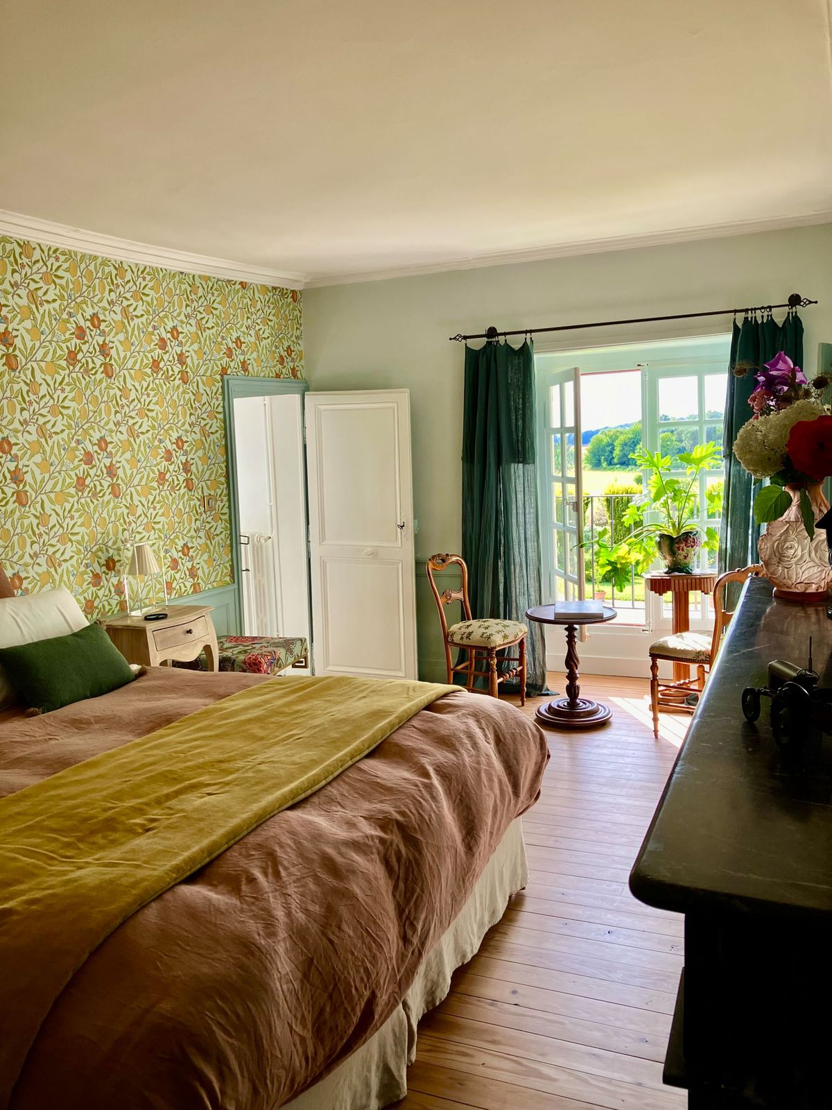 Guest bedroom with botanical wallpaper, dusty rose bedding, and French doors opening to countryside