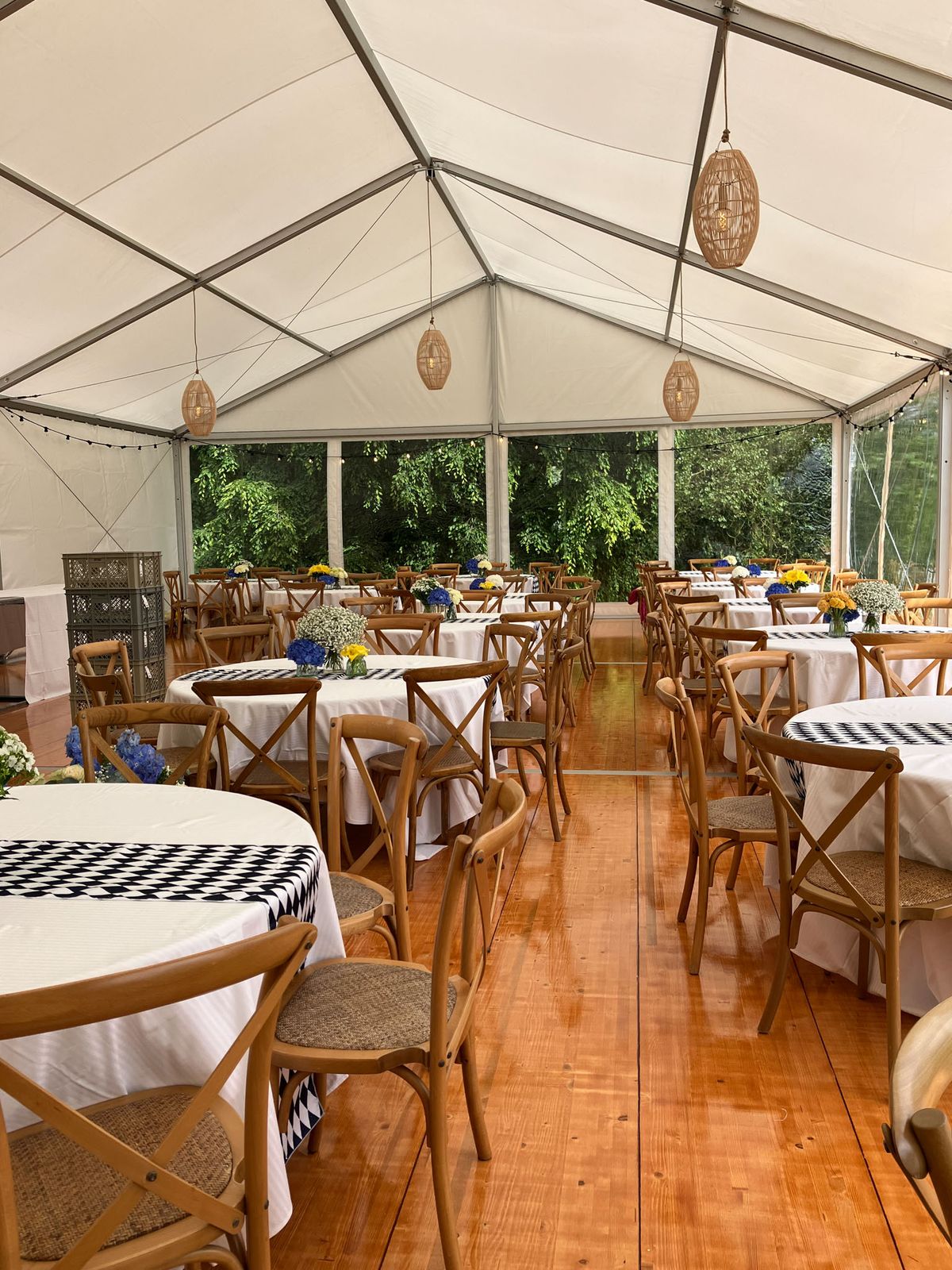 Marquee reception with round tables, cross-back chairs, blue hydrangea centerpieces, and rattan pendant lanterns