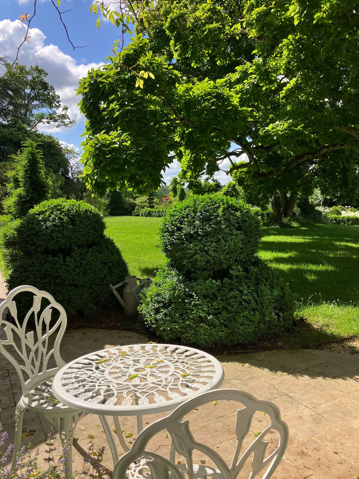 White iron bistro table and chairs on a stone terrace overlooking a manicured garden with boxwood hedges