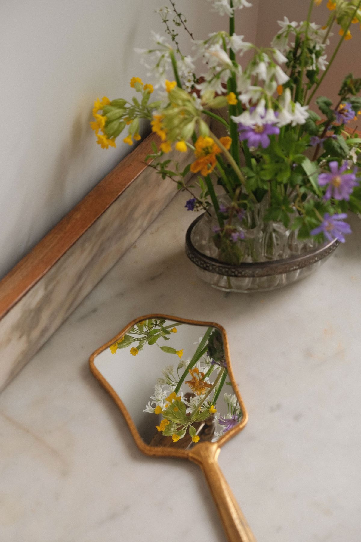 Wildflower arrangement in silver vessel with gold vintage hand mirror on marble surface
