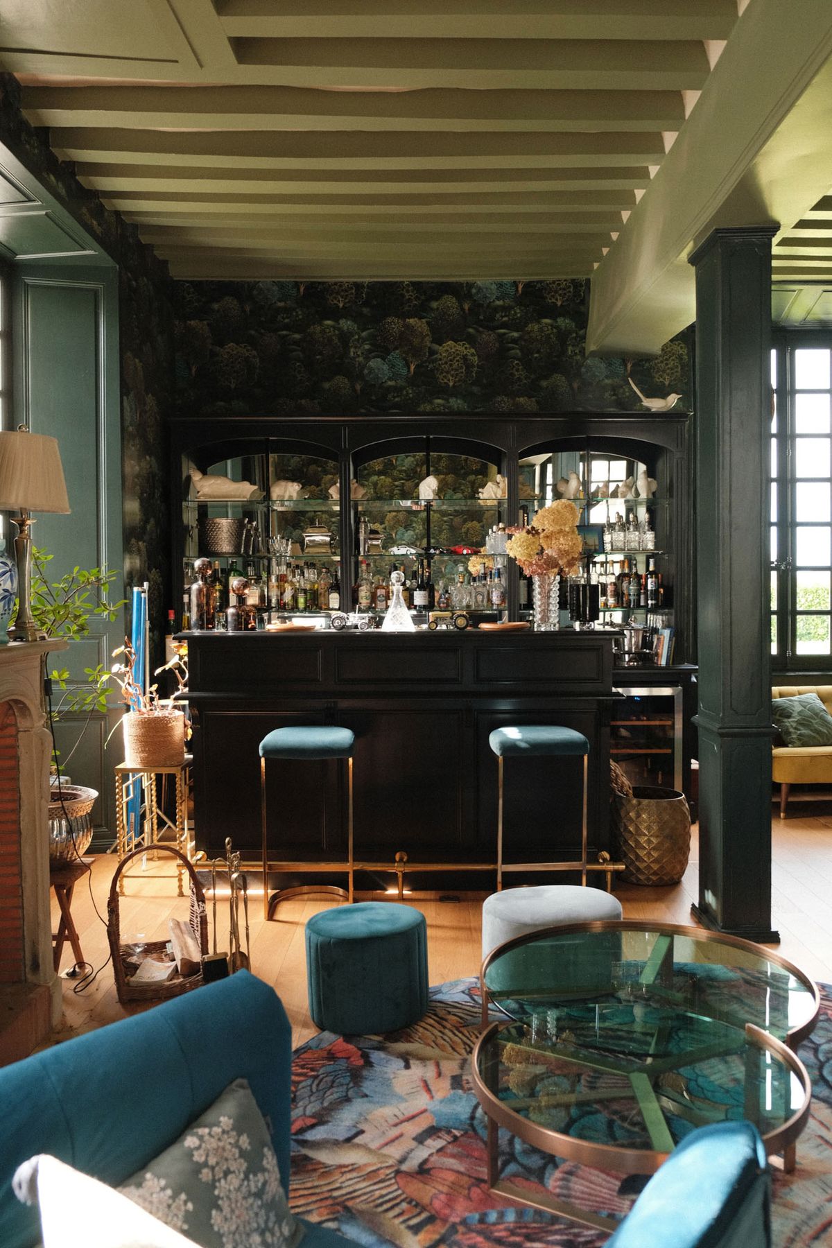 Maximalist bar with teal velvet stools, deep green walls, botanical wallpaper, and black lacquered cabinet