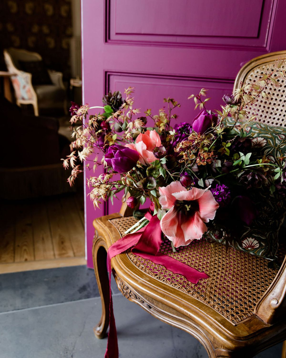 Jewel-tone bouquet of purple tulips, coral parrot tulips, and magenta anemones on cane-back chair