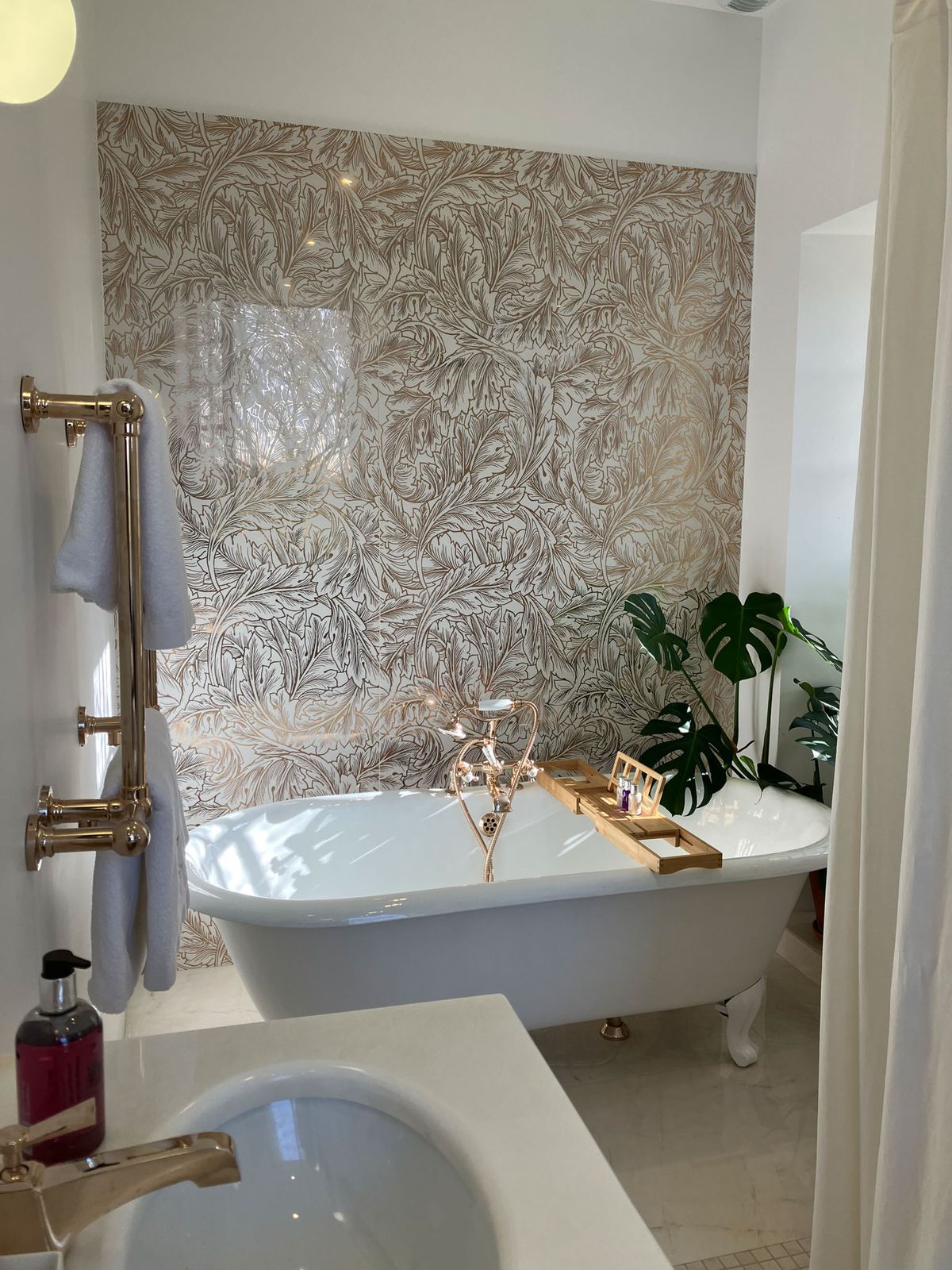 Bathroom with white clawfoot tub botanical wallpaper rose gold fittings and monstera plant