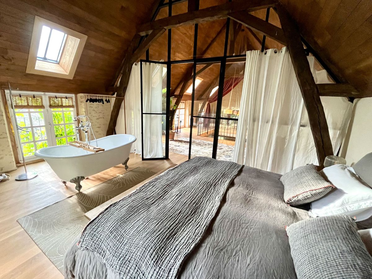 Converted barn suite with timber beam vault, freestanding claw-foot tub, glass partition, and skylight windows