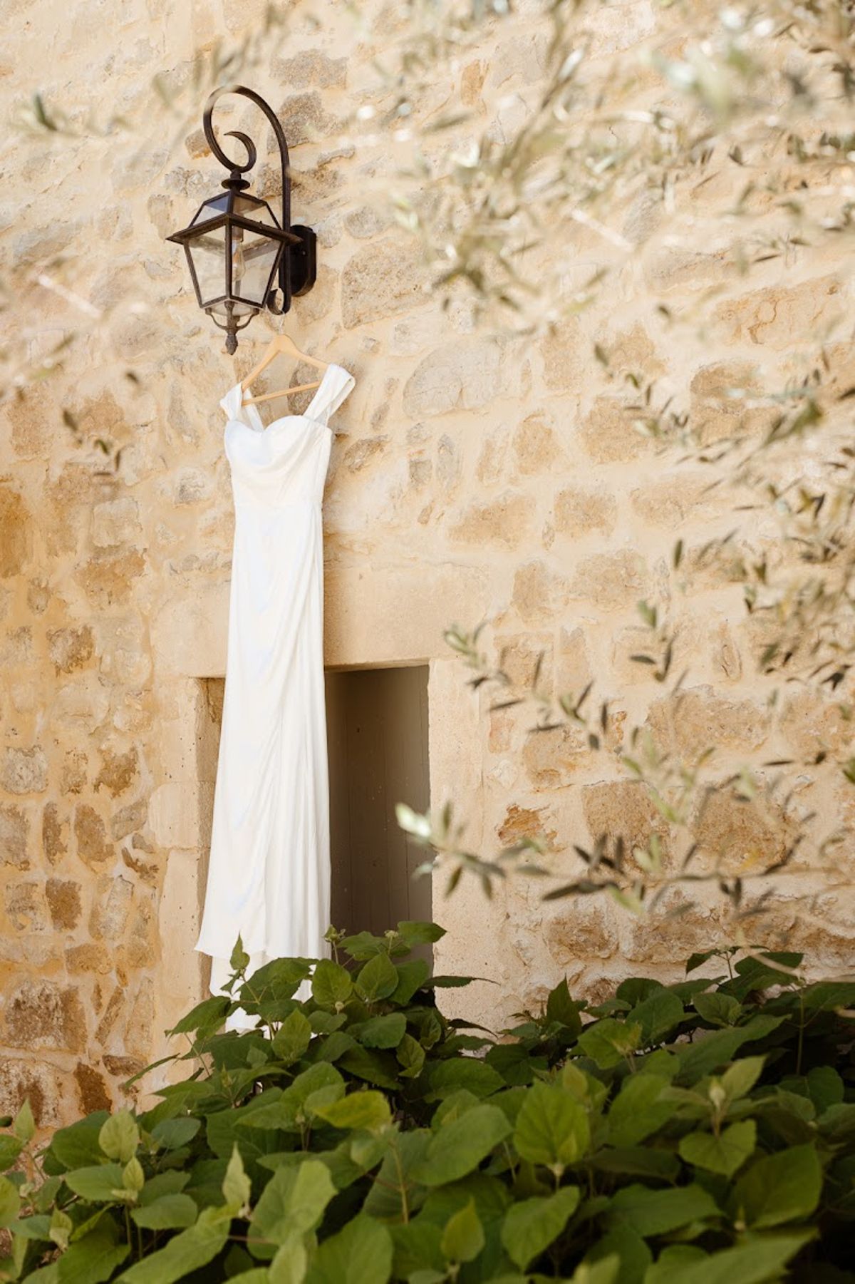 Ivory crepe column dress with sweetheart neckline hanging from iron lantern on honey stone wall