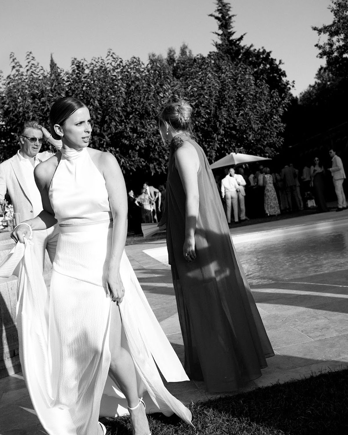 Black and white candid of bride in halter gown walking through terrace cocktail hour gathering