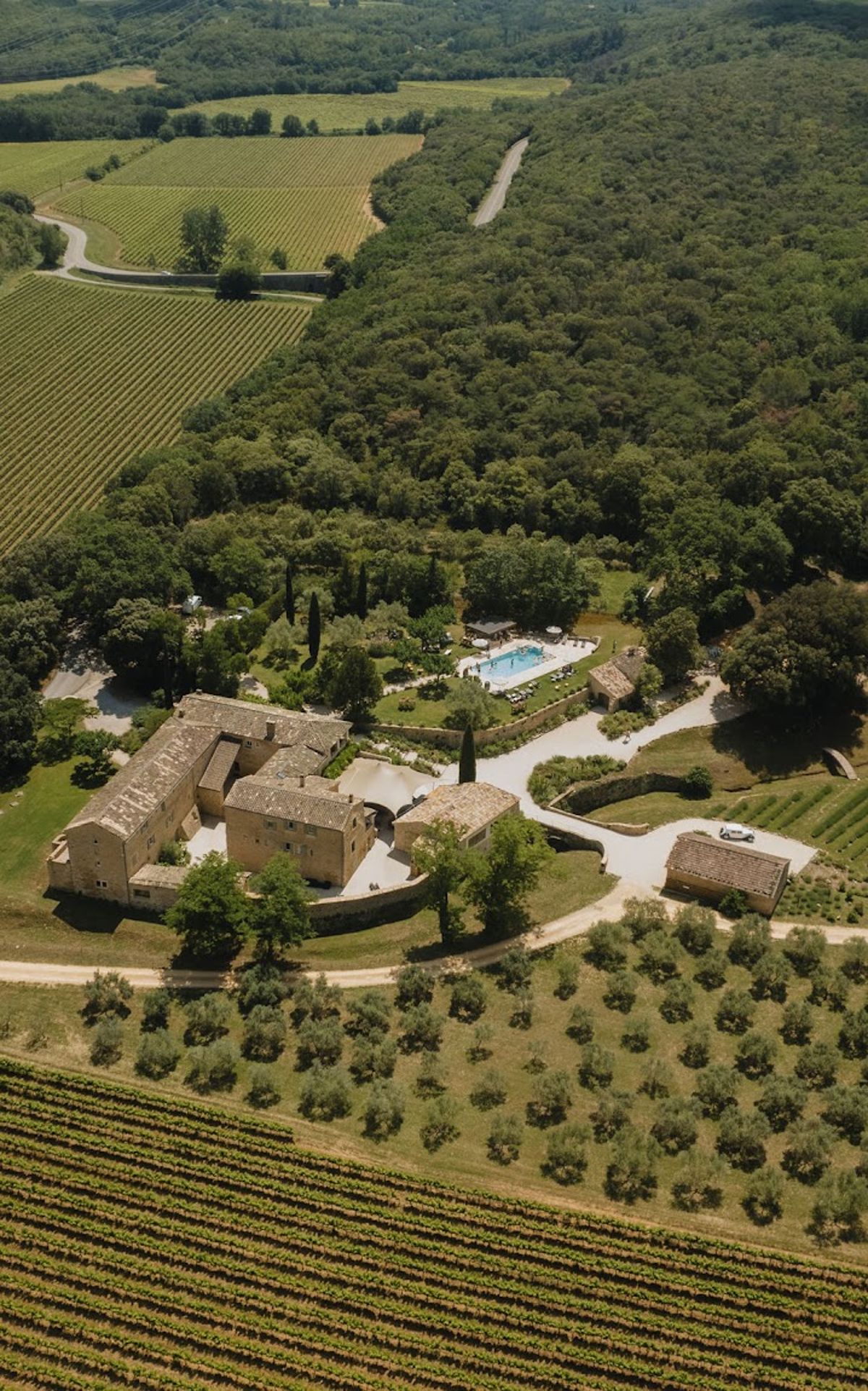 Aerial view of golden stone Provencal mas estate with pool, vineyards, and olive grove surroundings