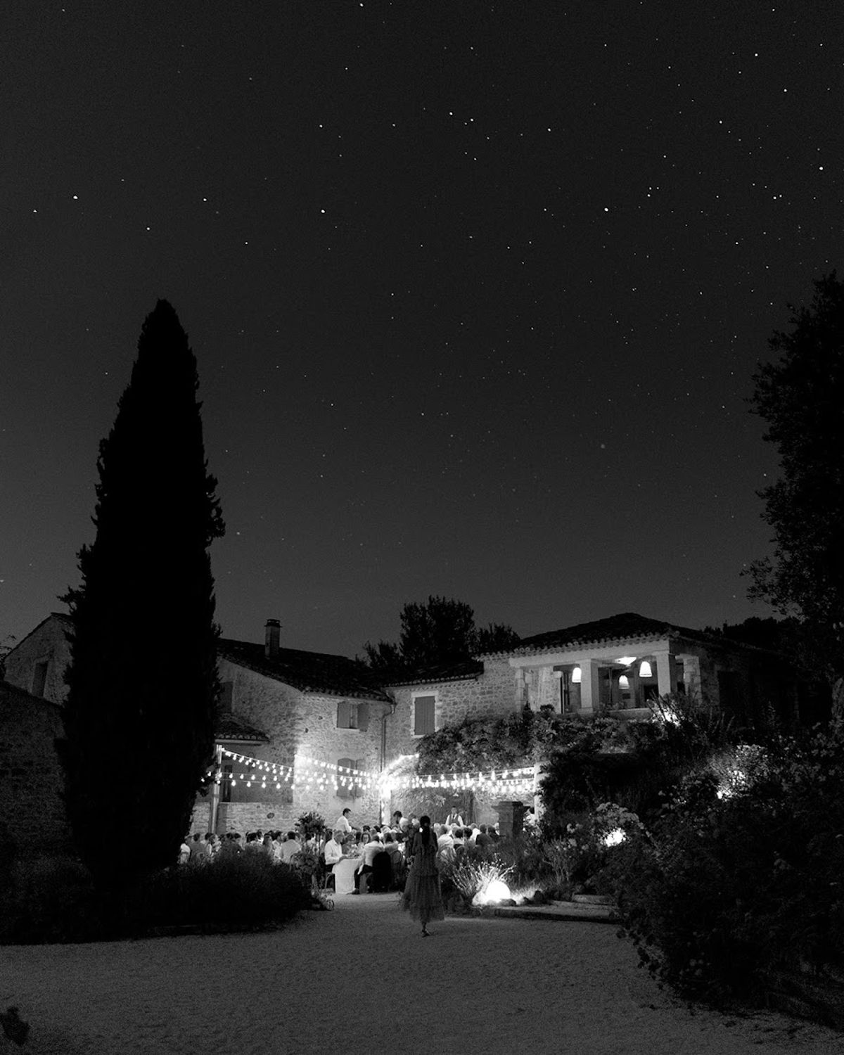 Night reception under festoon lights at stone mas courtyard with starry sky and cypress silhouette in B&W