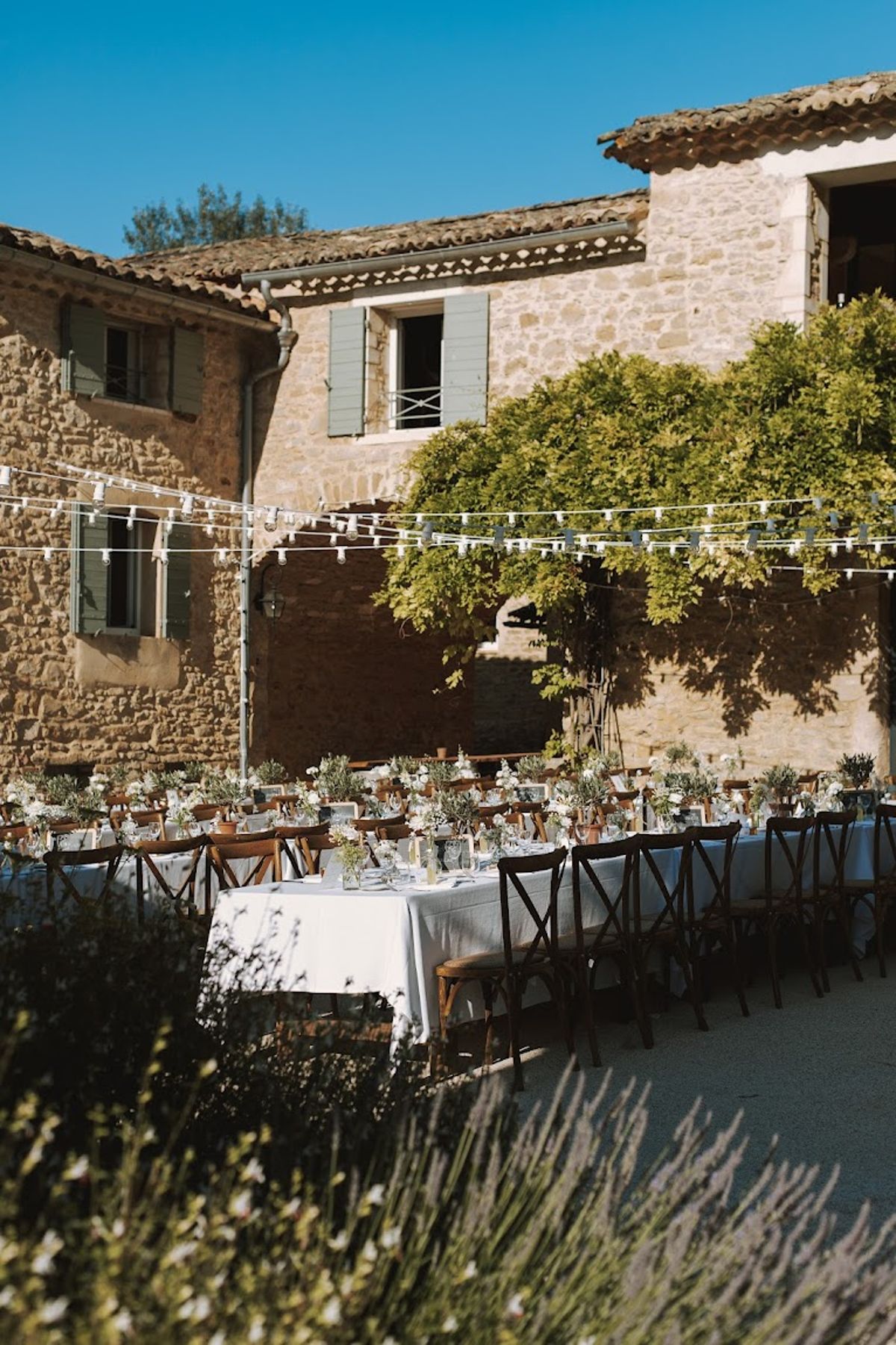 Courtyard reception at stone Provencal mas with banquet tables, cross-back chairs, and string lights overhead