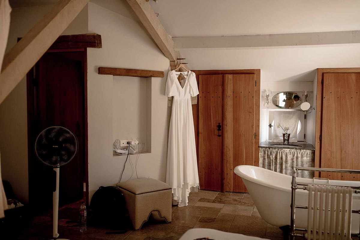 Ivory wedding dress hanging in rustic bridal suite with exposed wooden beams