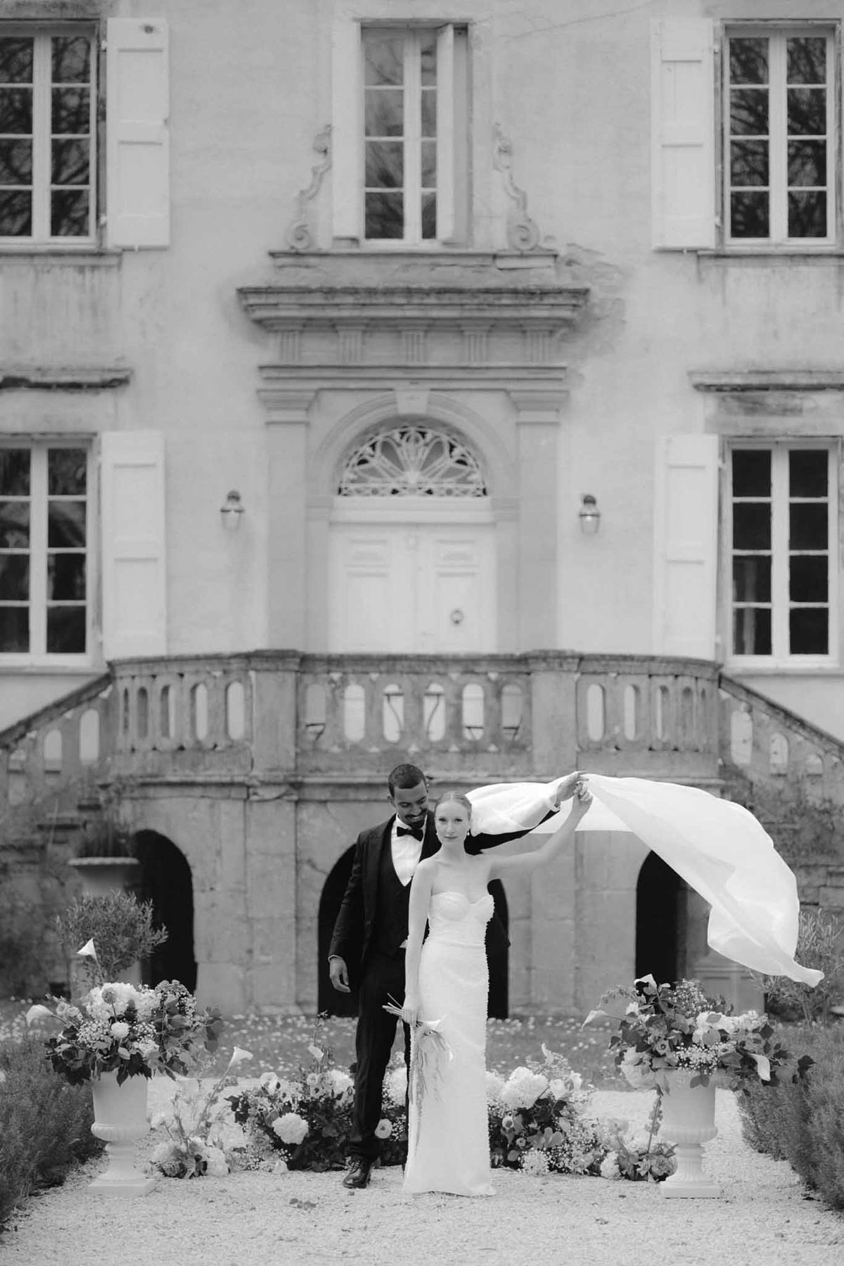 Bride and groom portrait in front of classical French château with floral arrangements
