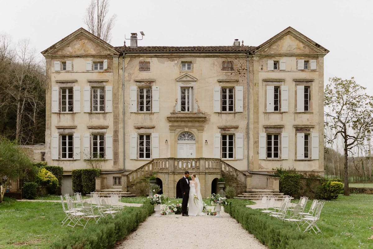 Bride and groom ceremony at French manor house with white chairs and formal courtyard