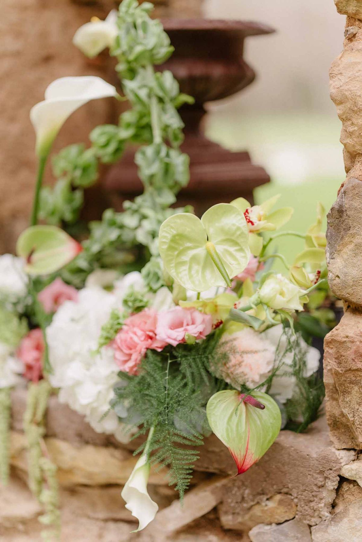 Bridal bouquet with white calla lilies and coral carnations against rustic stone wall