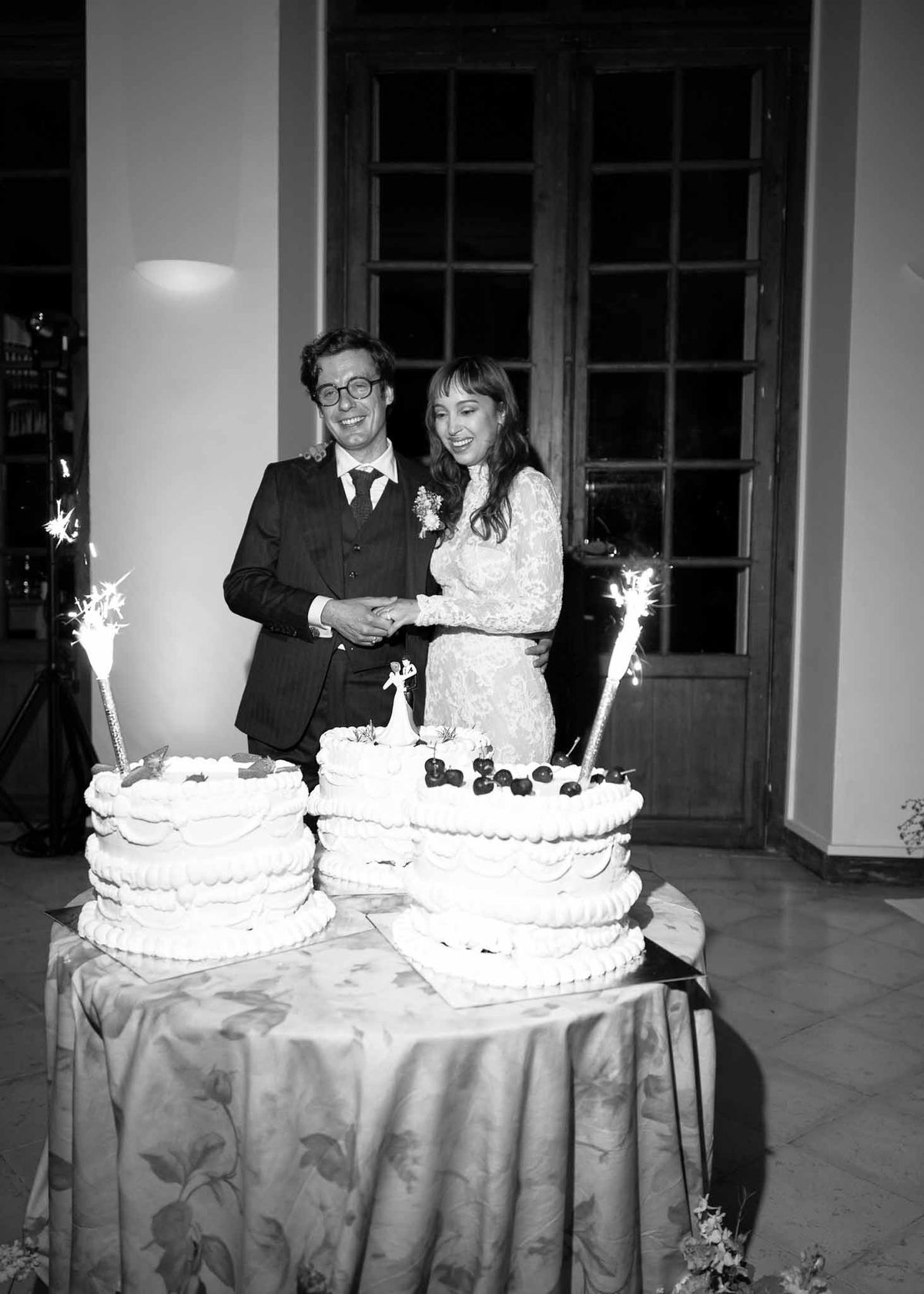 Bride and groom cutting wedding cake during indoor reception with sparklers and champagne